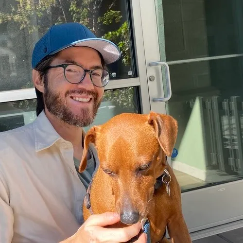 Ken smiling with Jack, a brown dog, at an outdoor café table